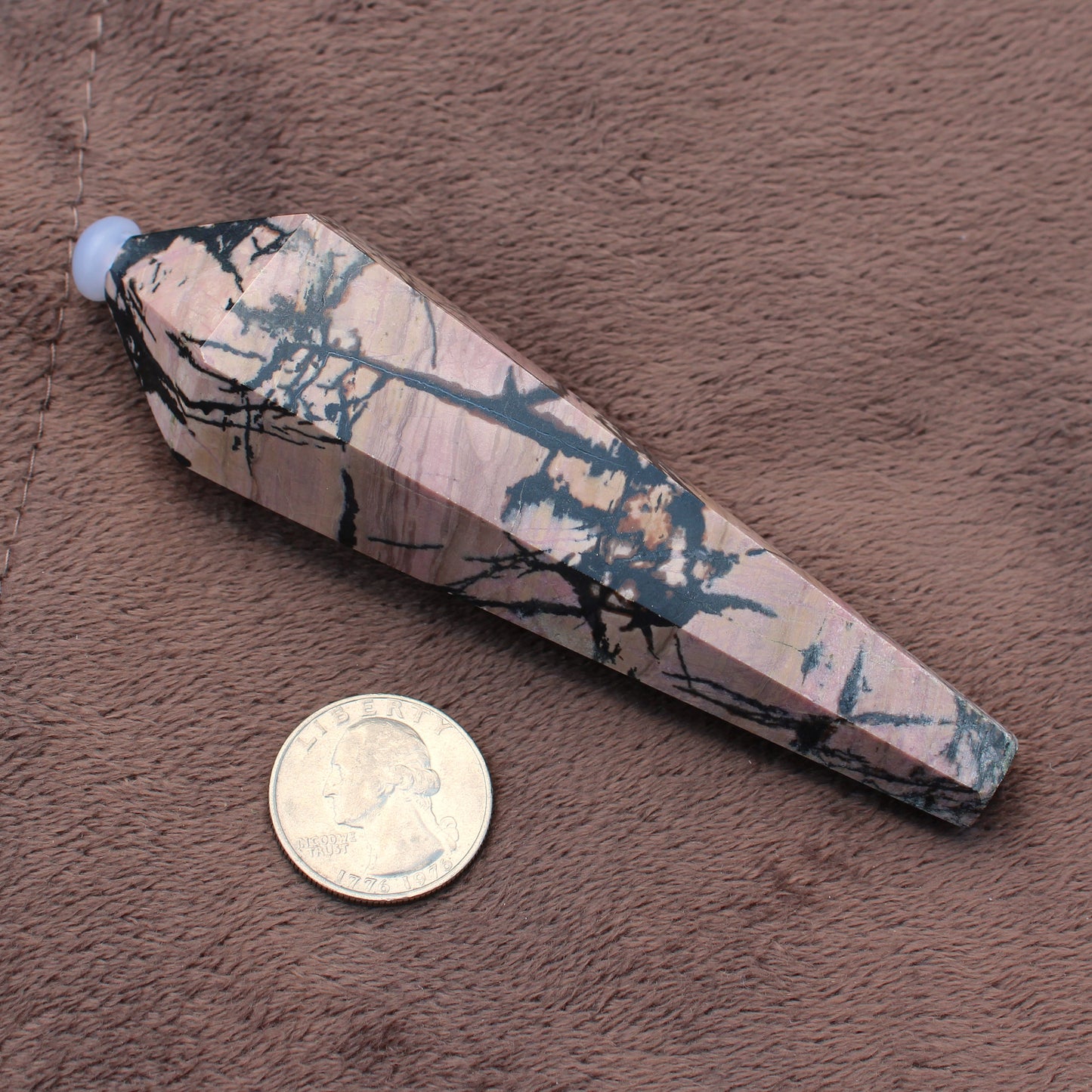 Rhodonite Wand crystal with black veining next to a US quarter for size reference
