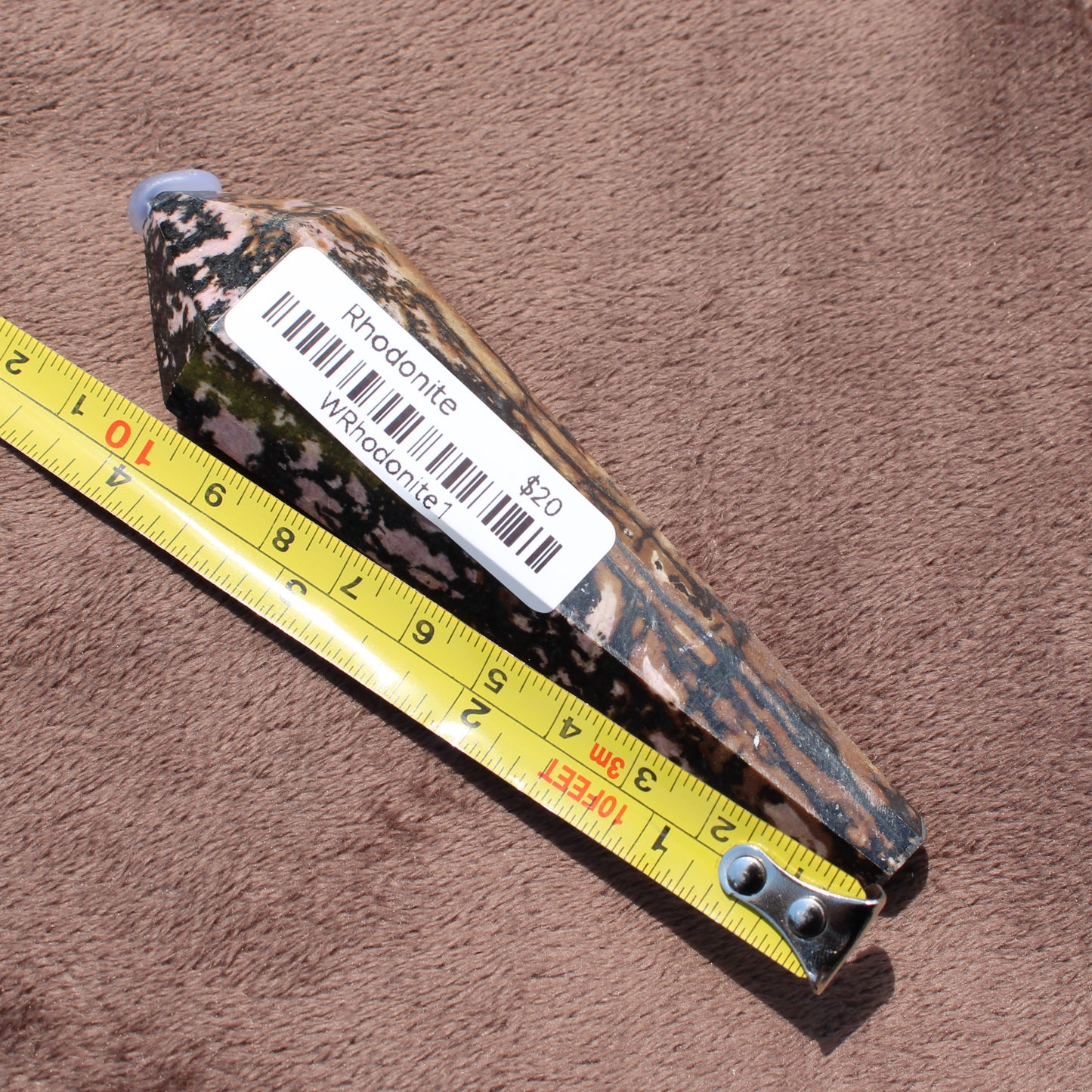 Rhodonite Wand crystal measuring about 9 inches with pink and black patterns on brown fabric
