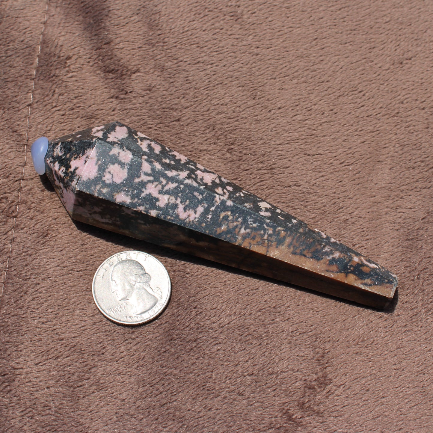 Polished Rhodonite Wand crystal with pink and black patterns displayed next to a US quarter for size comparison