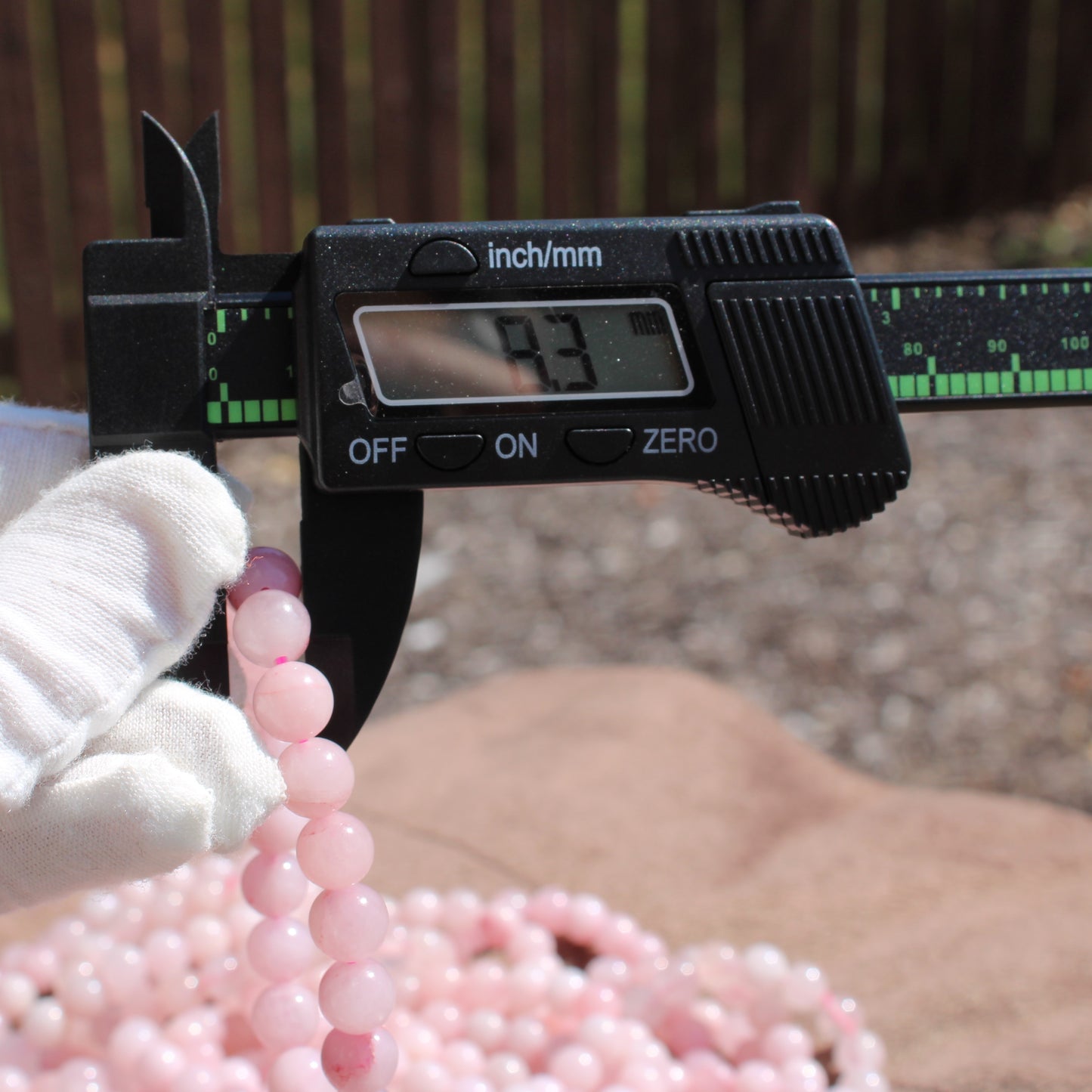 Measuring a Rose Quartz Bracelet with a caliper to show size and quality of the beads
