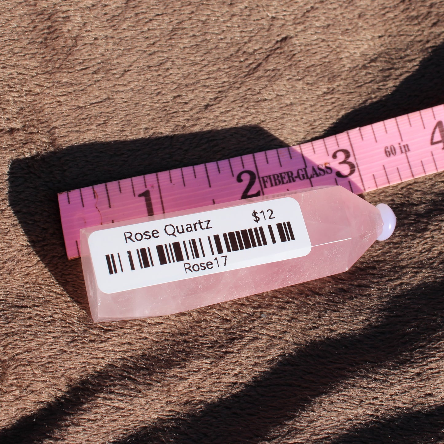Rose Quartz tower displayed next to a measuring ruler on a soft surface
