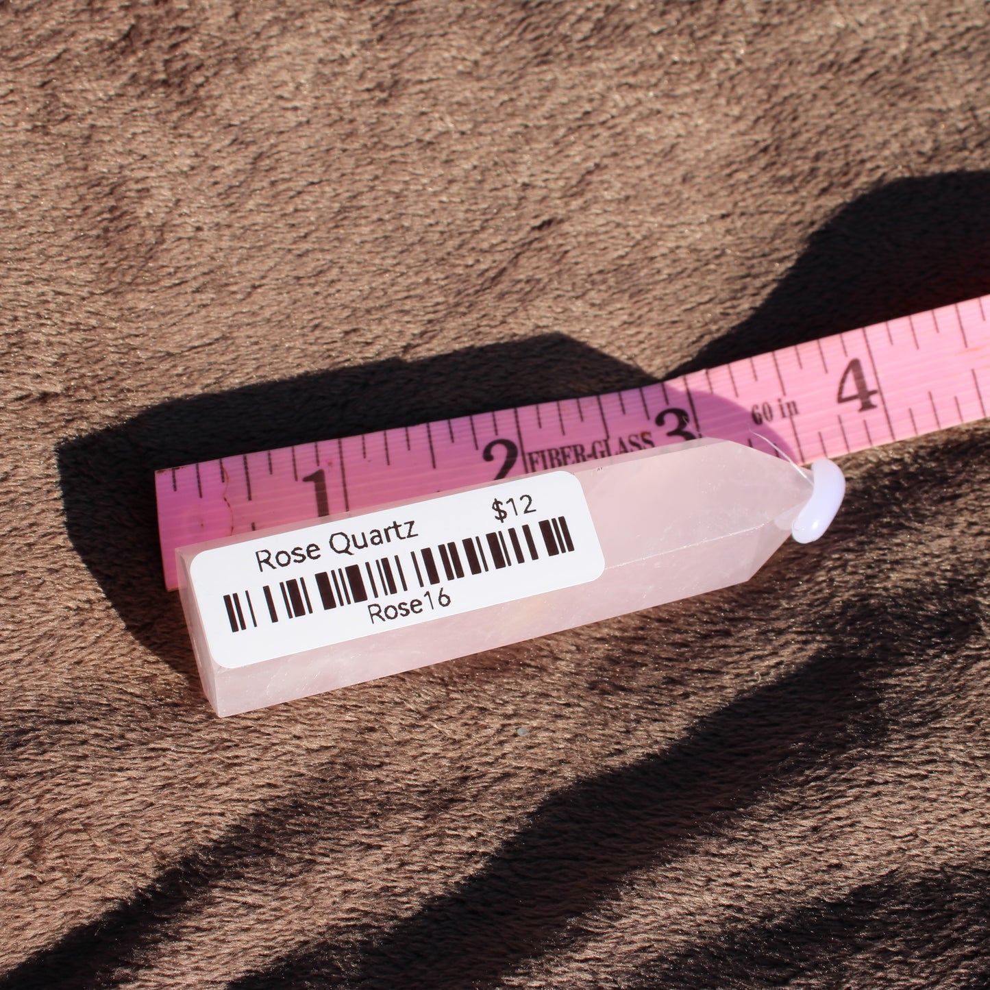Rose Quartz tower displayed on fabric with a ruler for size comparison