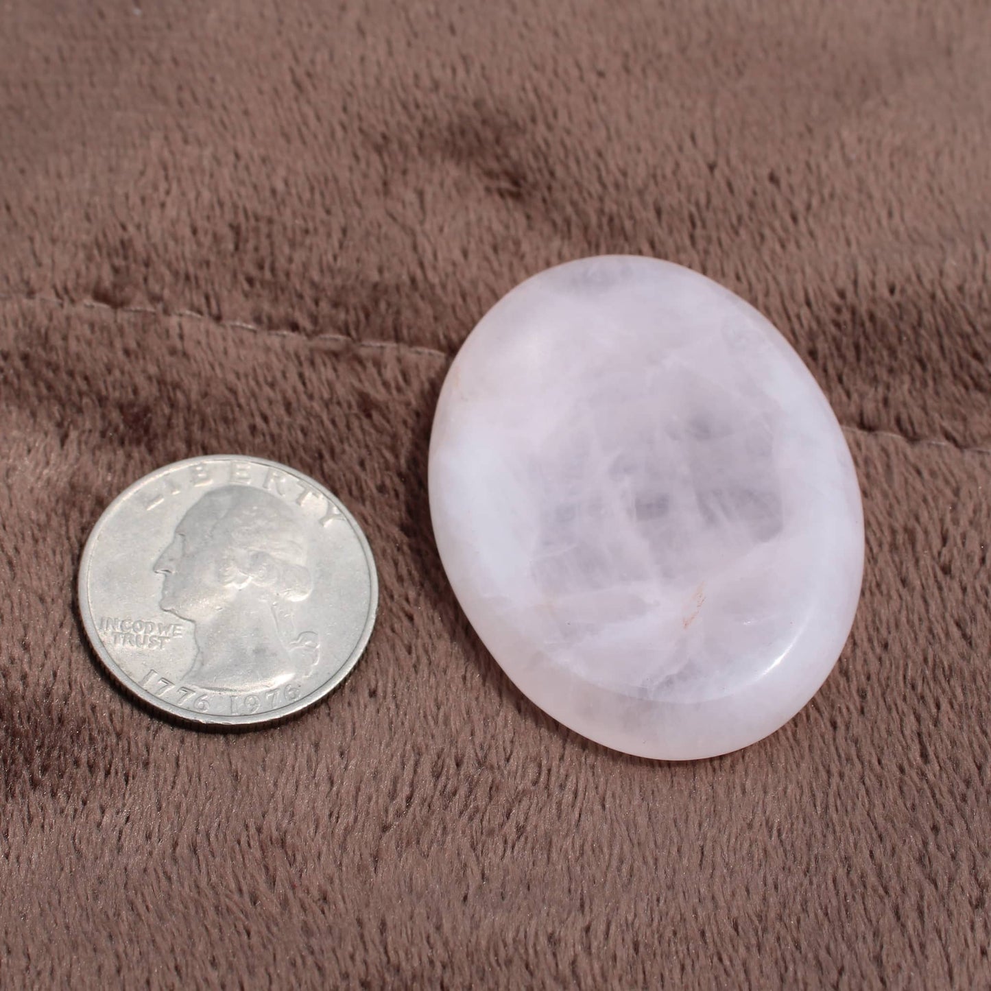 Rose Quartz Worry Stone next to a quarter on a brown textured surface by Different Branches LLC