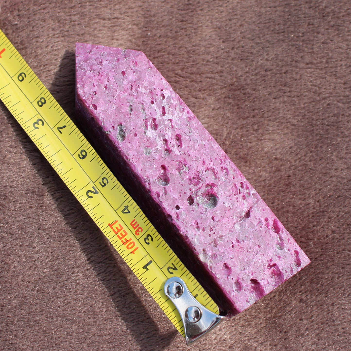 Ruby Tower crystal with textured pink surface placed next to yellow measuring tape showing size