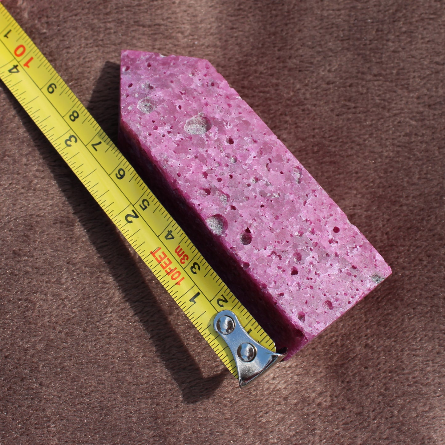 Ruby Tower pink crystal stone with textured surface next to a measuring tape showing its size