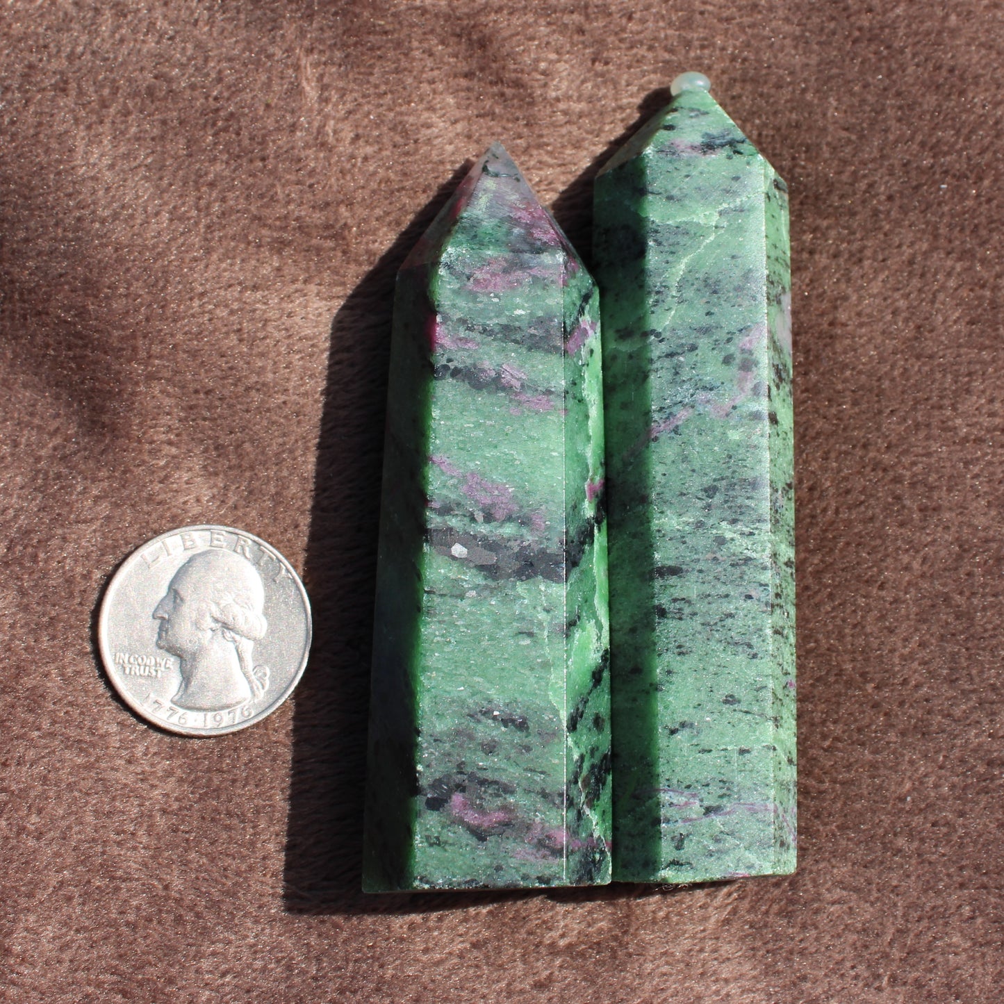 Two polished Ruby Zoisite Tower crystals beside a US quarter for size comparison on brown fabric
