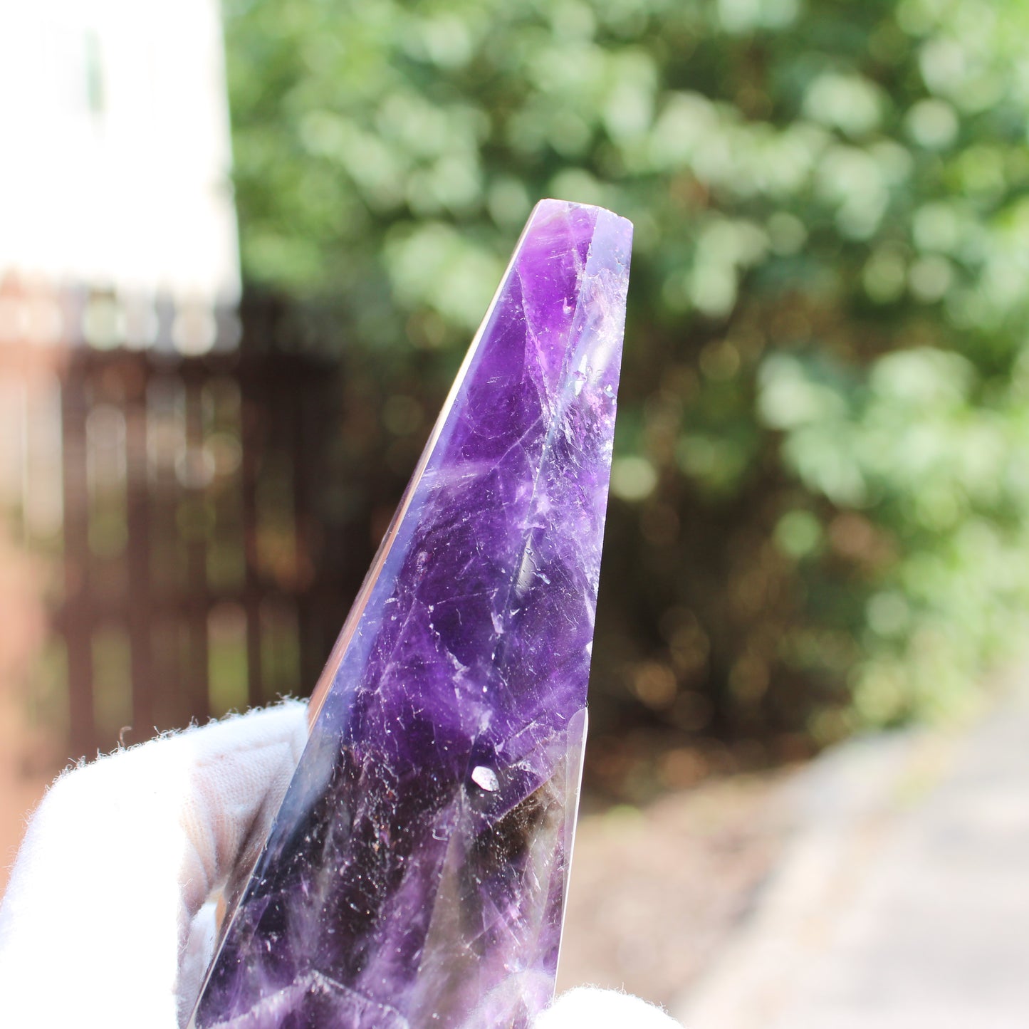 Close-up of Thick Amethyst Wand crystal held by hand outdoors with blurred green background