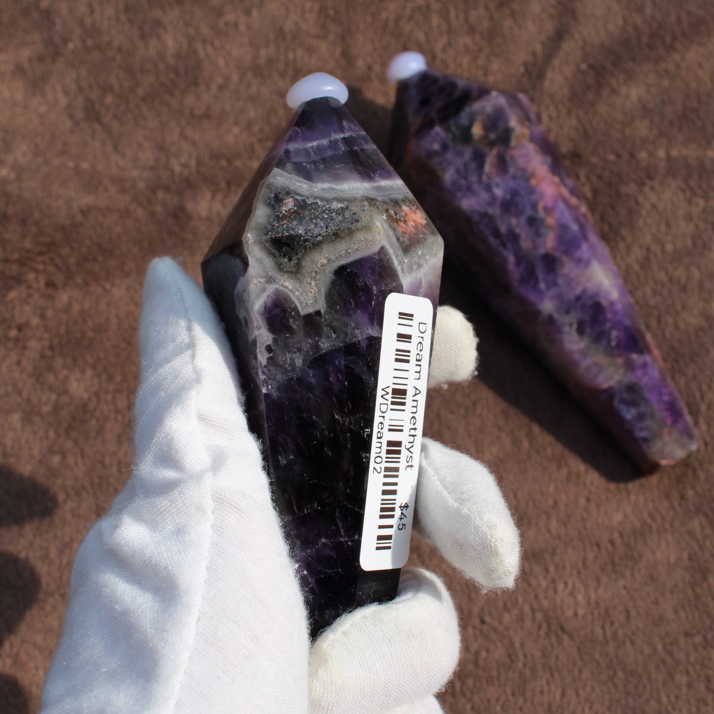 Hand holding a Thick Amethyst Wand crystal with purple and white banding by Different Branches LLC