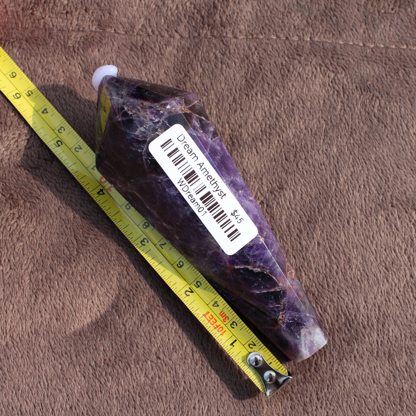 Thick Amethyst Wand crystal from Different Branches LLC placed next to measuring tape on brown fabric
