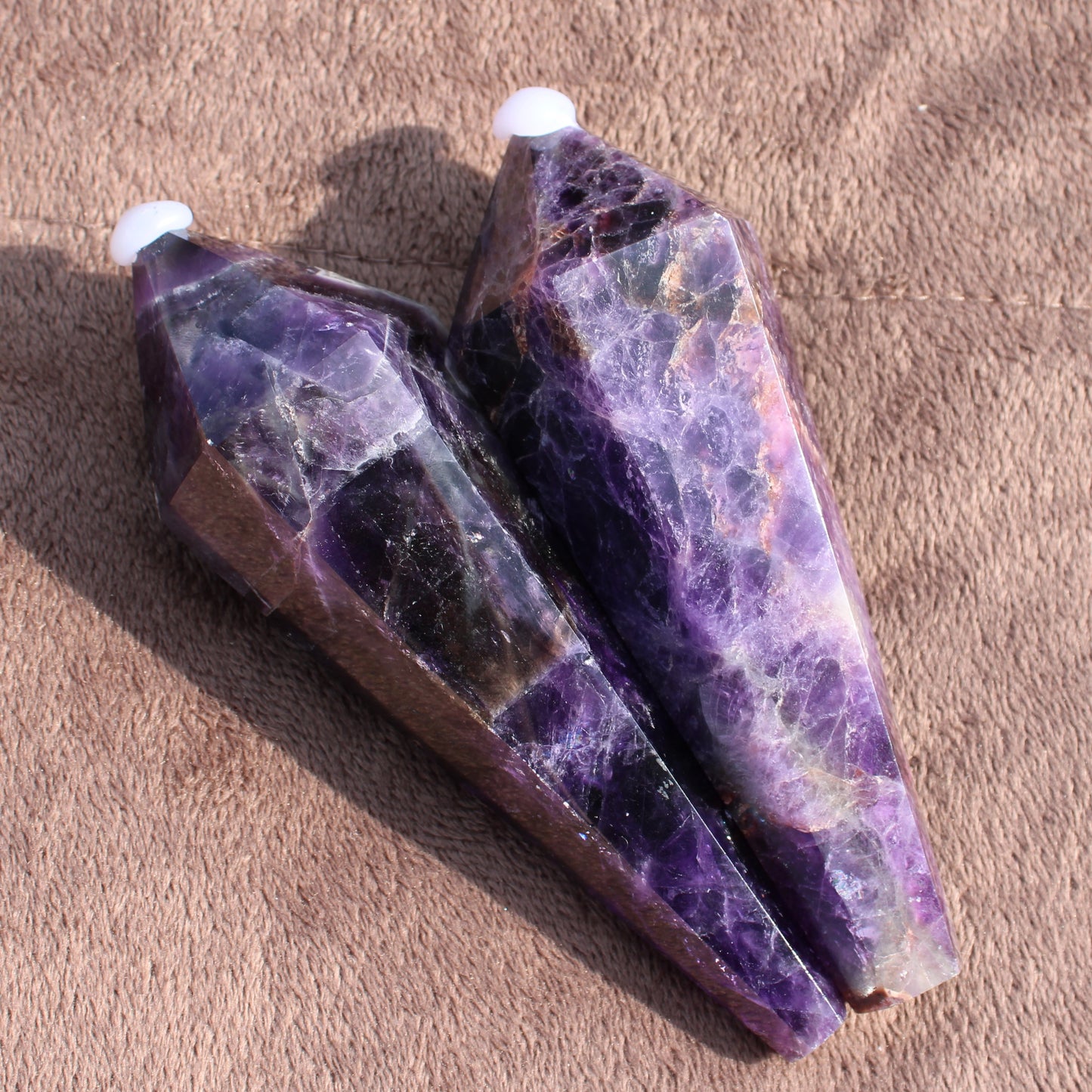 Two polished Thick Amethyst Wand crystals with deep purple hues on a textured brown surface