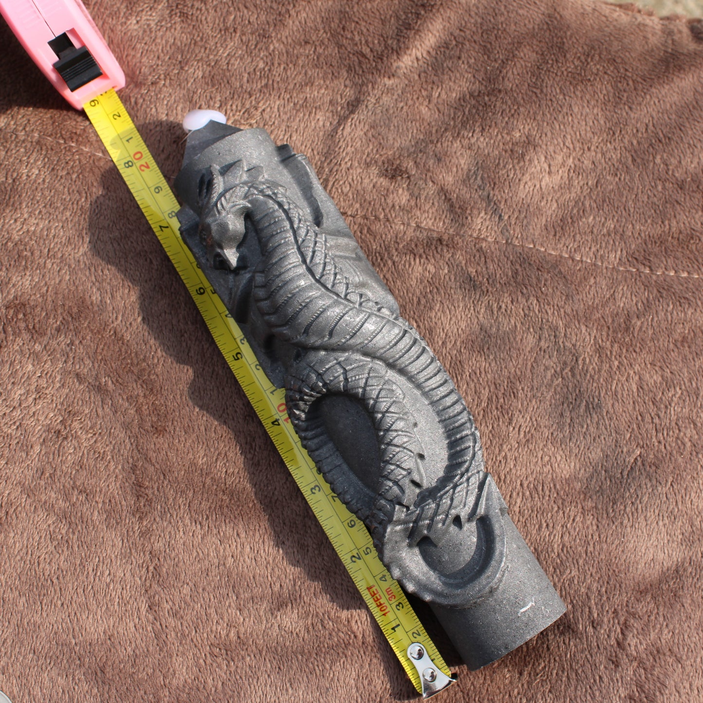 Shungite Dragon Tower crystal carved with detailed dragon design next to measuring tape on brown fabric