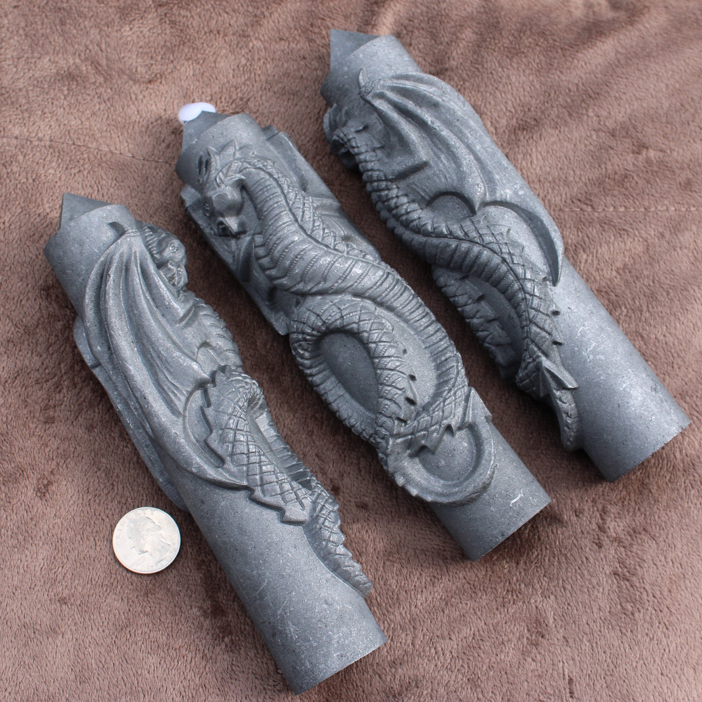 Three Shungite Dragon Tower crystal carvings displayed on a brown fabric with a coin for size reference