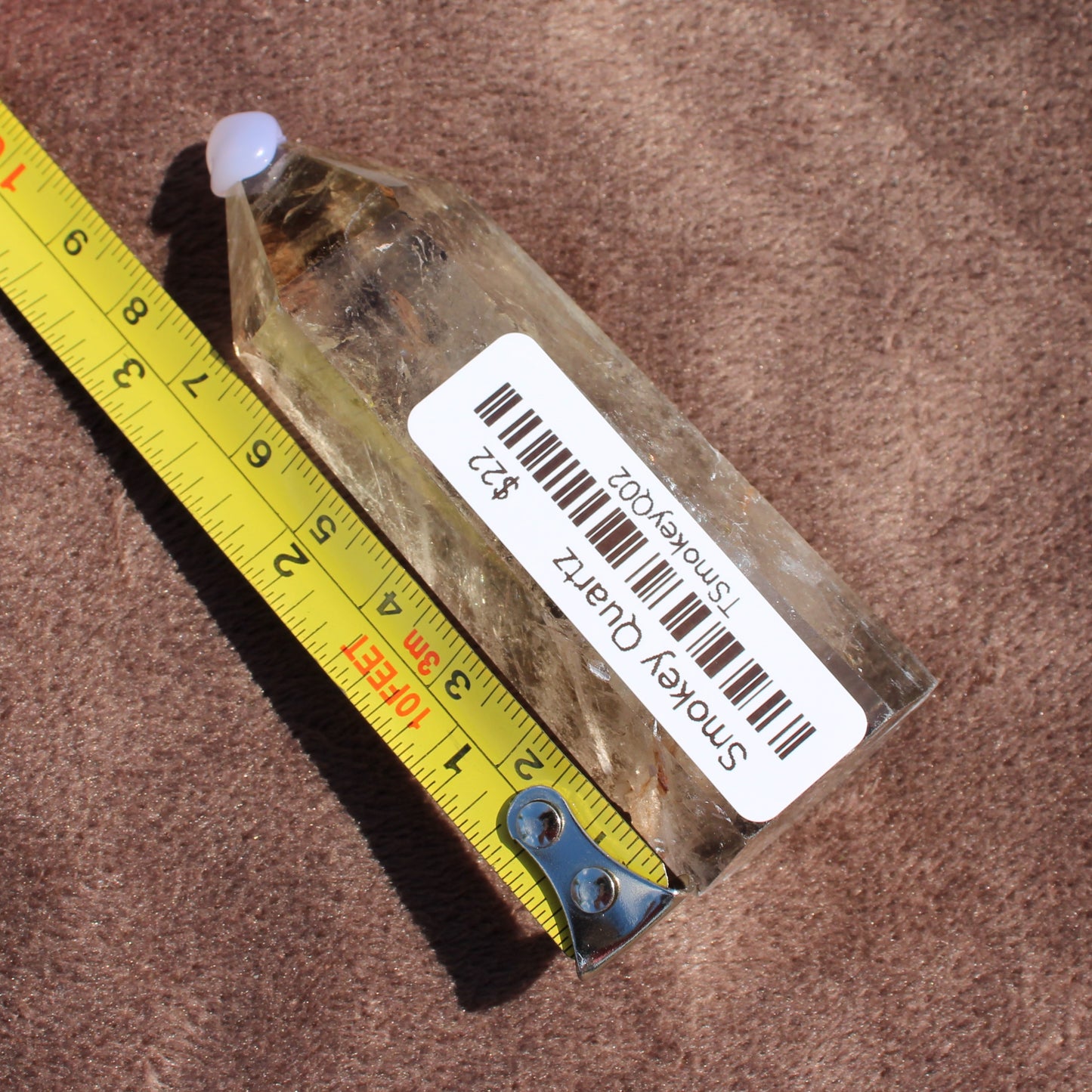 Smokey Quartz Tower crystal with measuring tape showing size on brown textured background