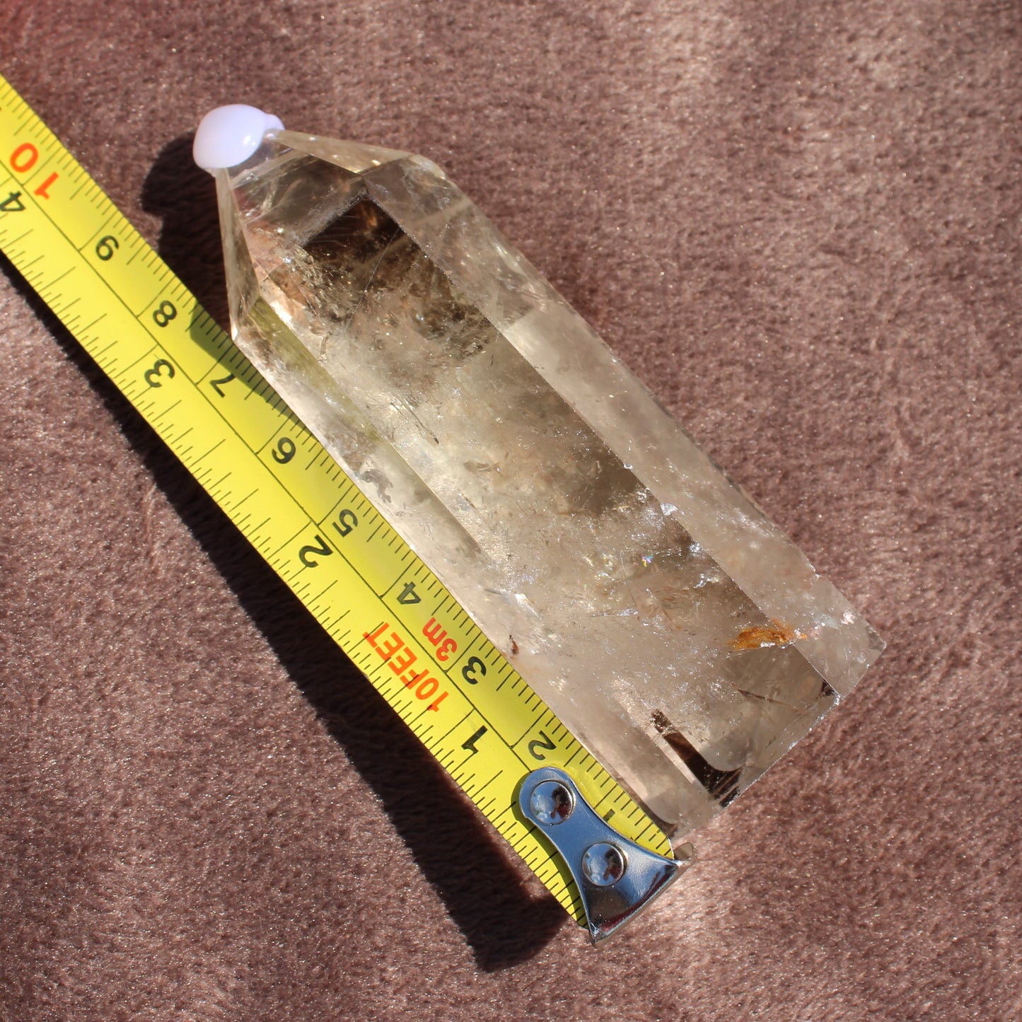 Smokey Quartz Tower crystal from Different Branches LLC displayed next to measuring tape on brown surface
