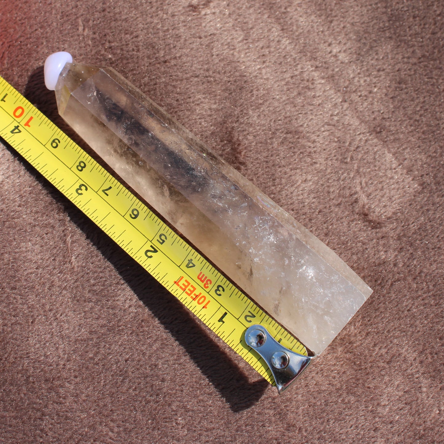 Clear Smokey Quartz Tower crystal placed next to a yellow measuring tape on brown fabric background