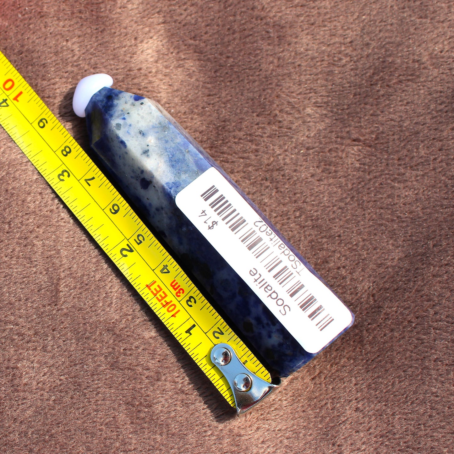 Sodalite Tower crystal from Different Branches LLC placed next to a yellow measuring tape on brown fabric