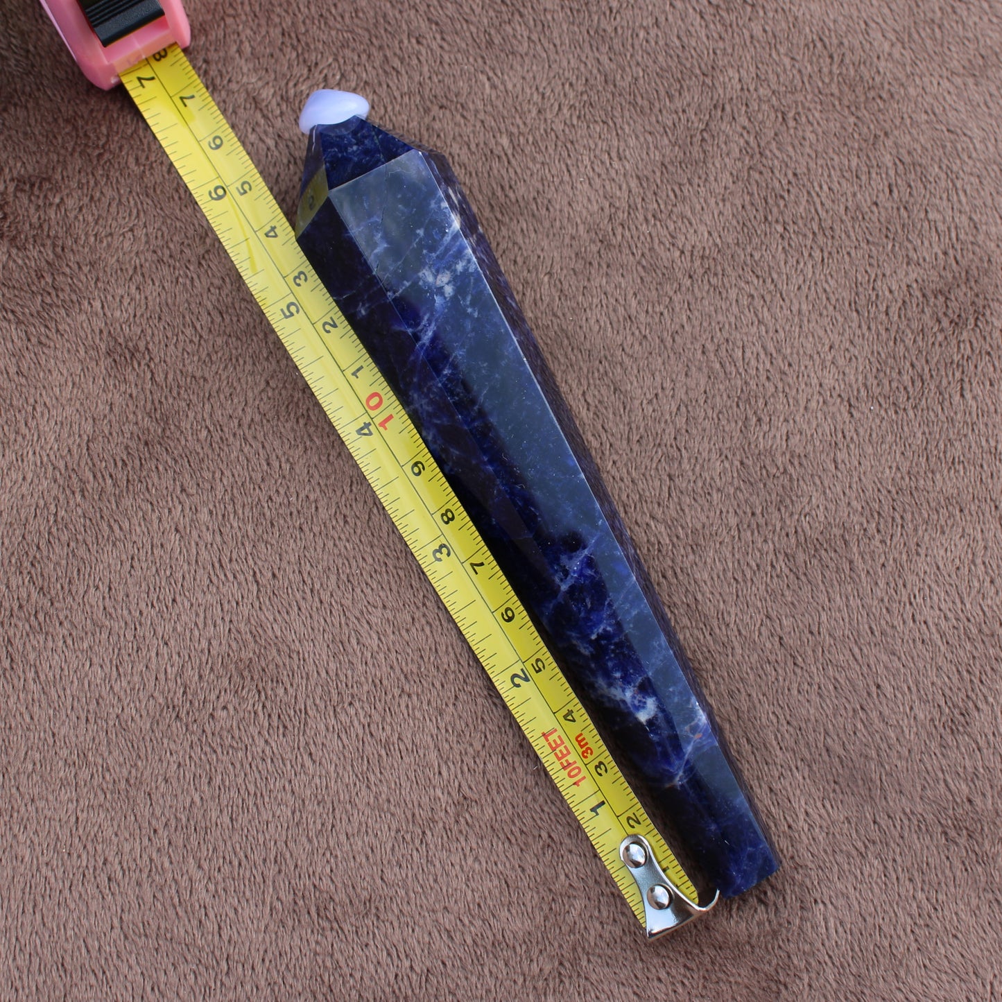 Deep blue Sodalite Wand crystal with pointed tip measured next to a tape measure on brown fabric