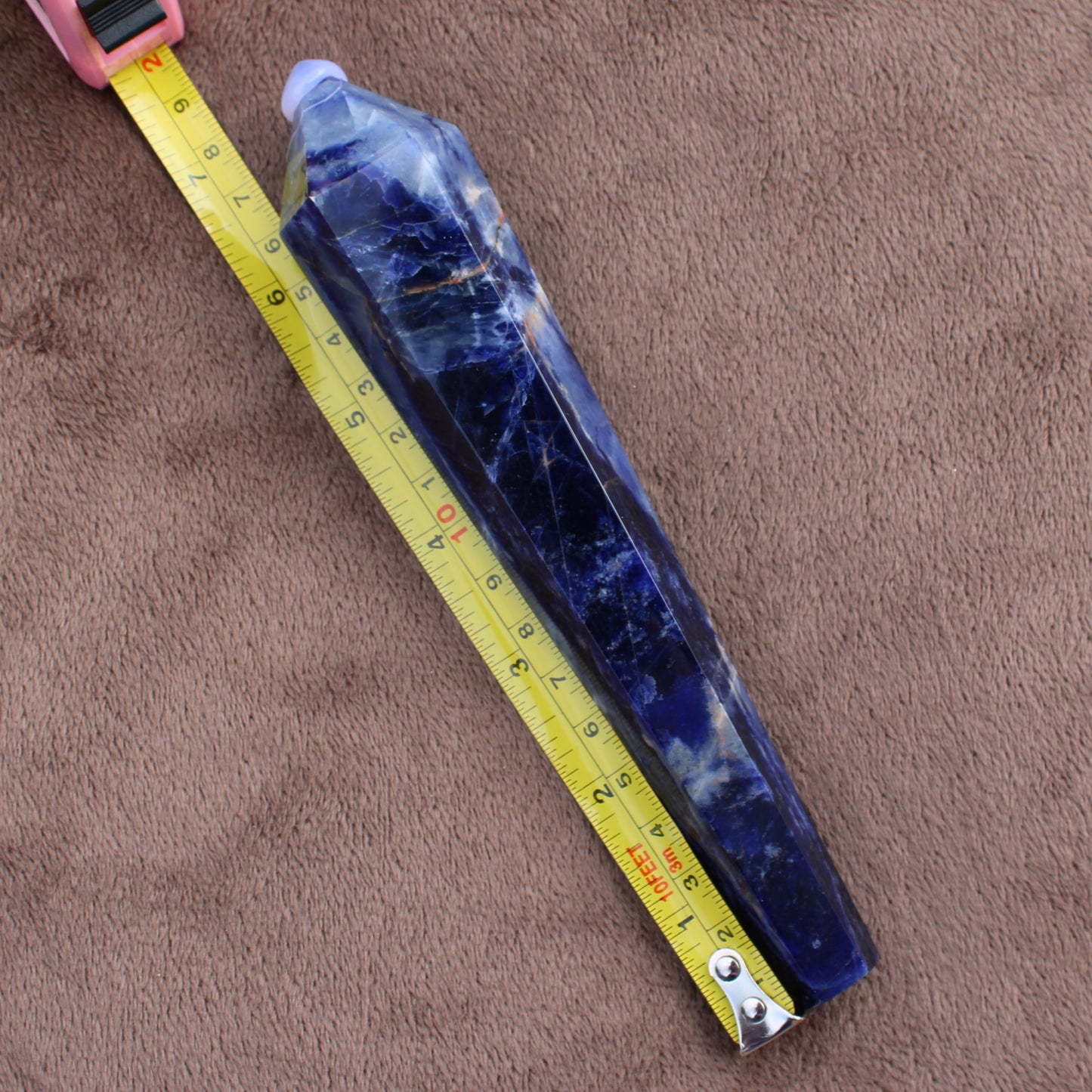 Sodalite Wand crystal from Different Branches LLC placed on brown surface next to a yellow measuring tape