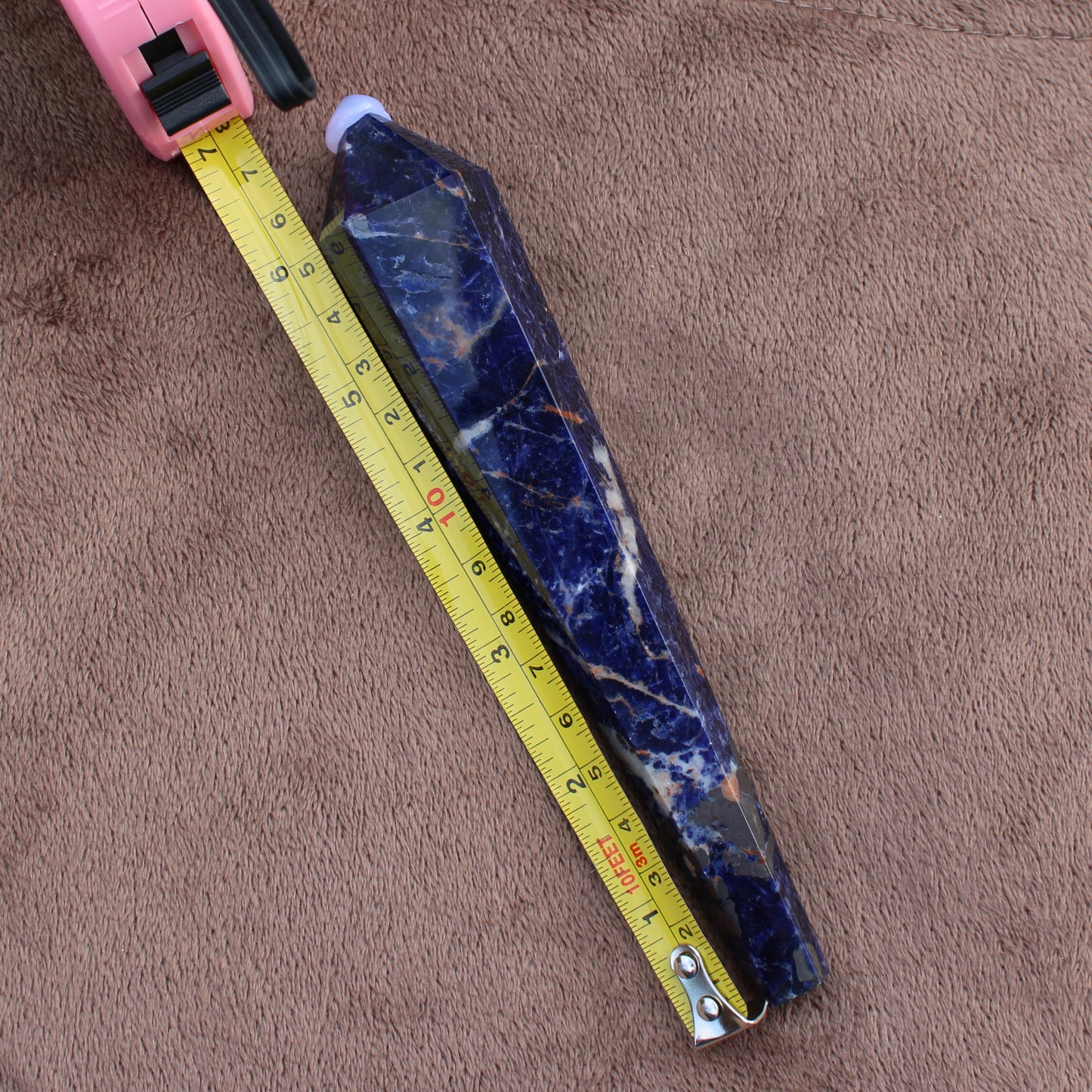 Sodalite Wand crystal measuring approximately 7 inches placed next to a yellow tape measure on brown fabric