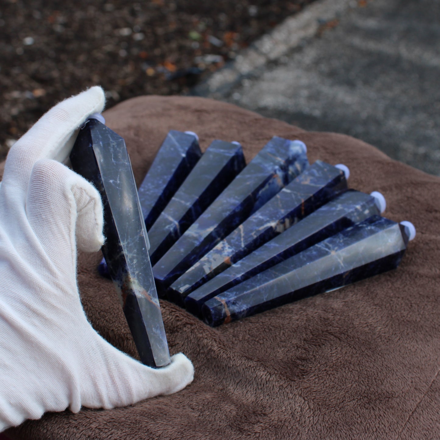 Hand holding a polished Sodalite Wand with multiple Sodalite Wands laid out on a brown cloth