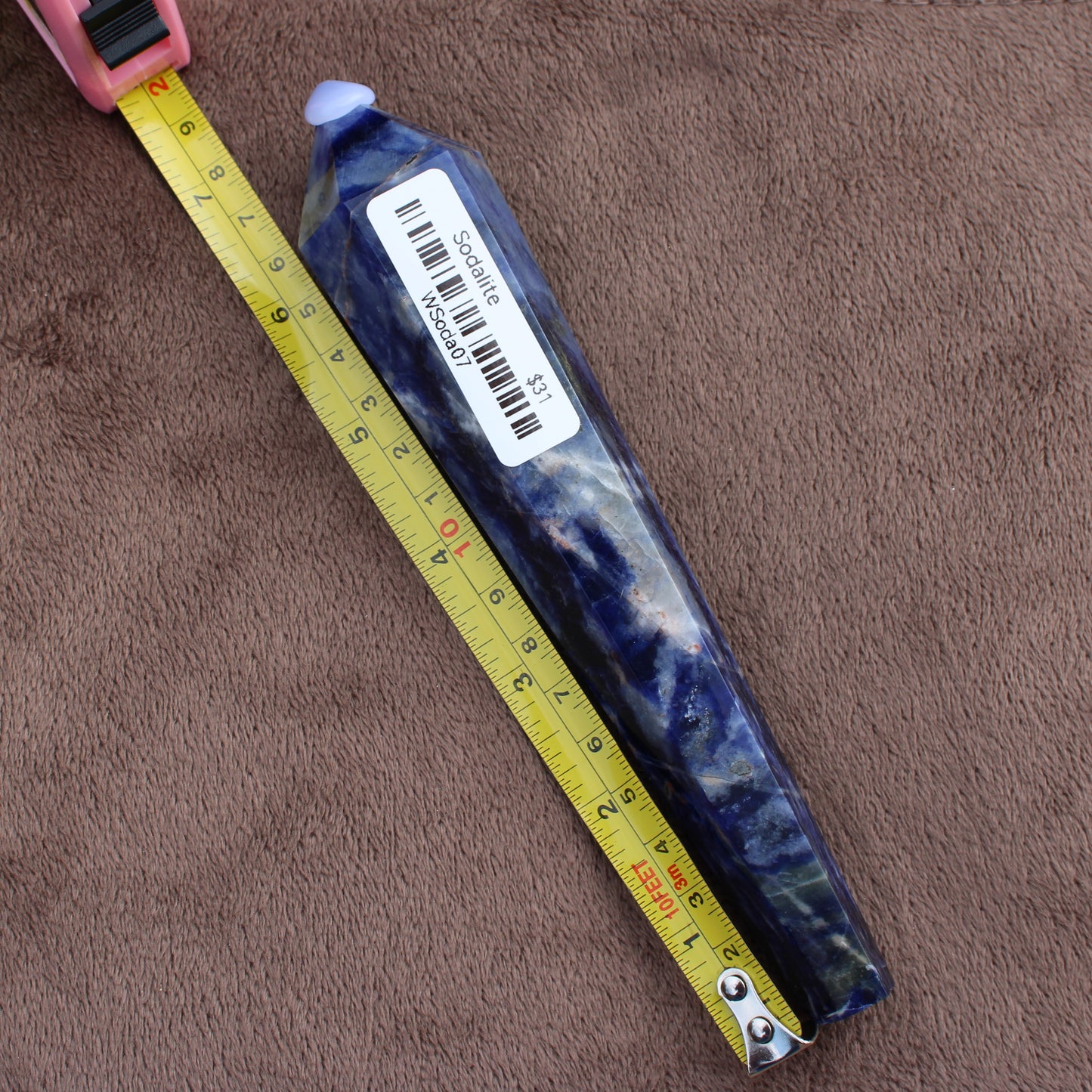Sodalite Wand crystal from Different Branches LLC placed beside measuring tape showing length on brown background
