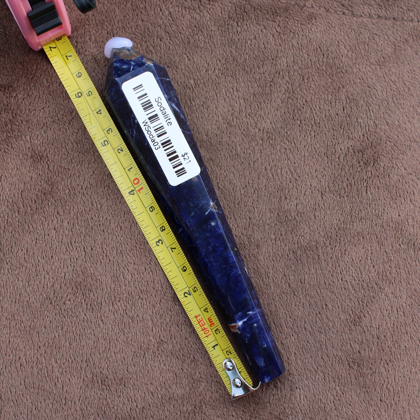 Sodalite wand crystal from Different Branches LLC placed next to a yellow measuring tape on brown fabric