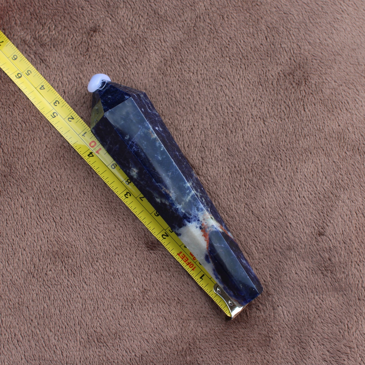 Sodalite Wand crystal from Different Branches LLC lying next to measuring tape on brown fabric