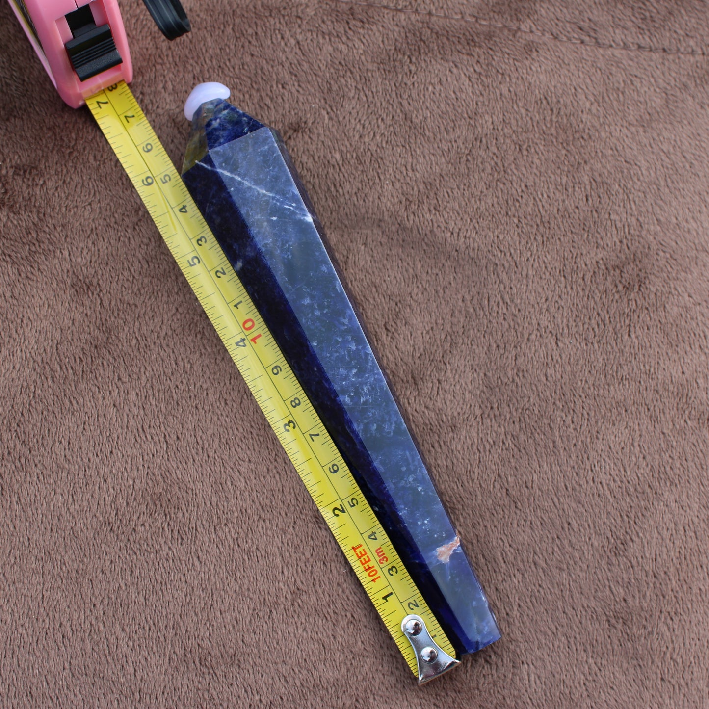 Sodalite Wand crystal with deep blue color placed next to a measuring tape on a brown fabric background