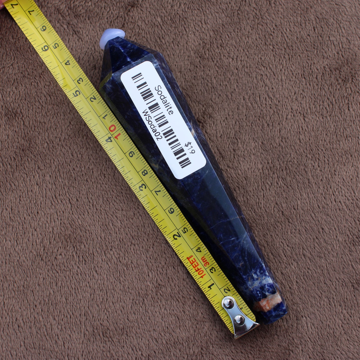 Sodalite Wand crystal from Different Branches LLC placed next to a measuring tape on a brown surface