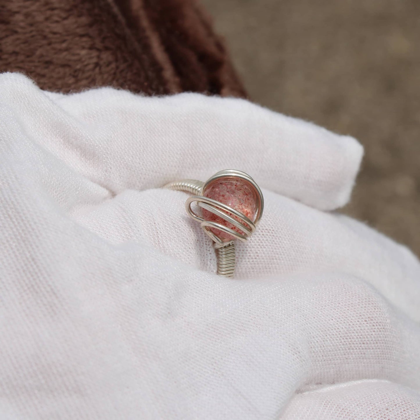 Strawberry quartz ring in silver setting held gently, showcasing its unique color and shine