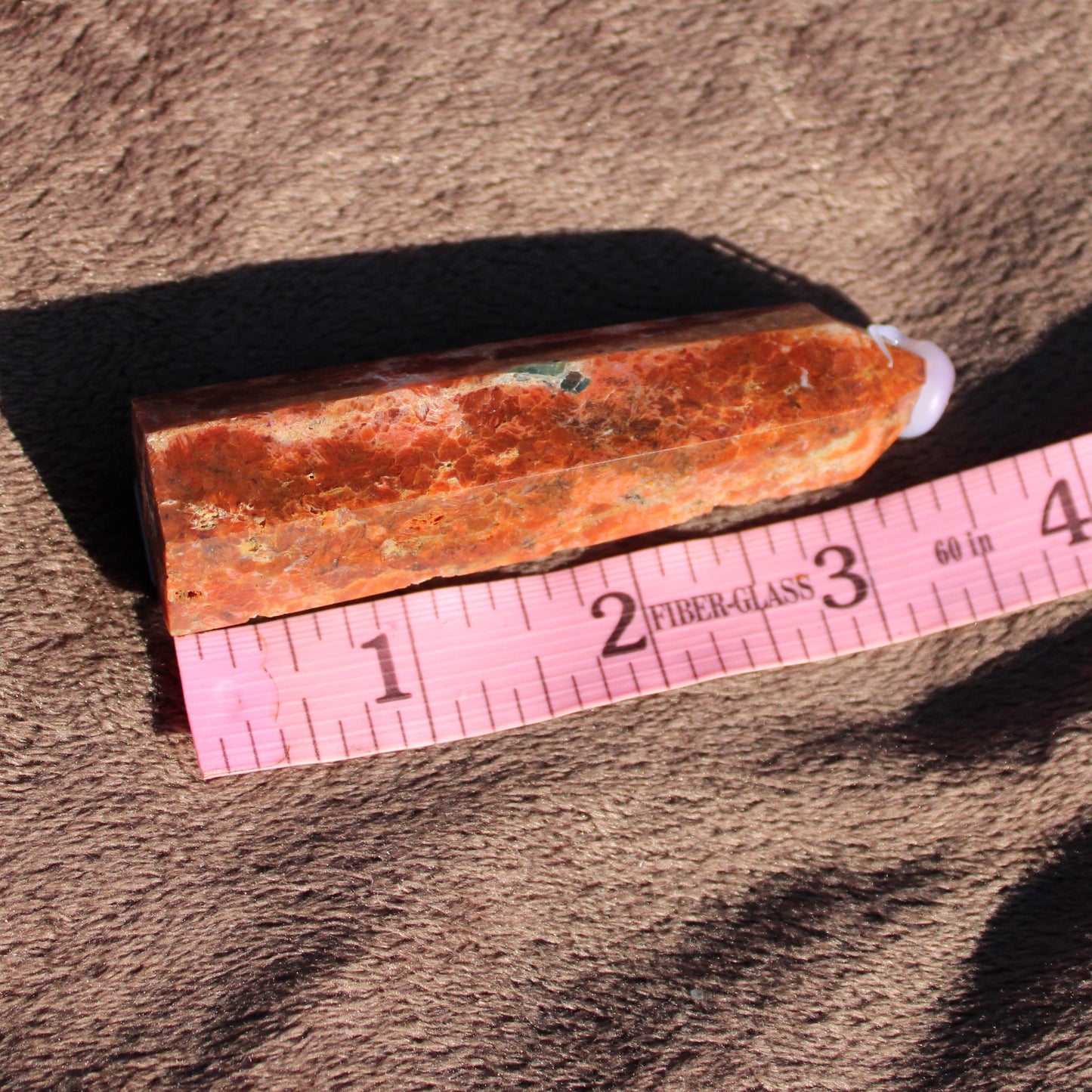 Sunstone tower with a polished orange surface measured against a ruler for size reference
