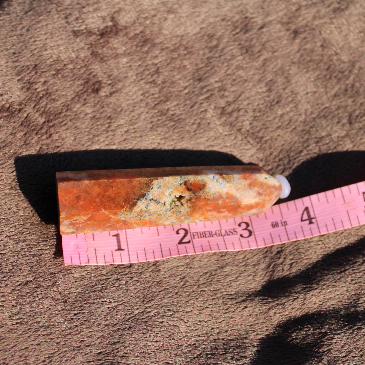 Sunstone tower crystal with vibrant orange hues on textured fabric background
