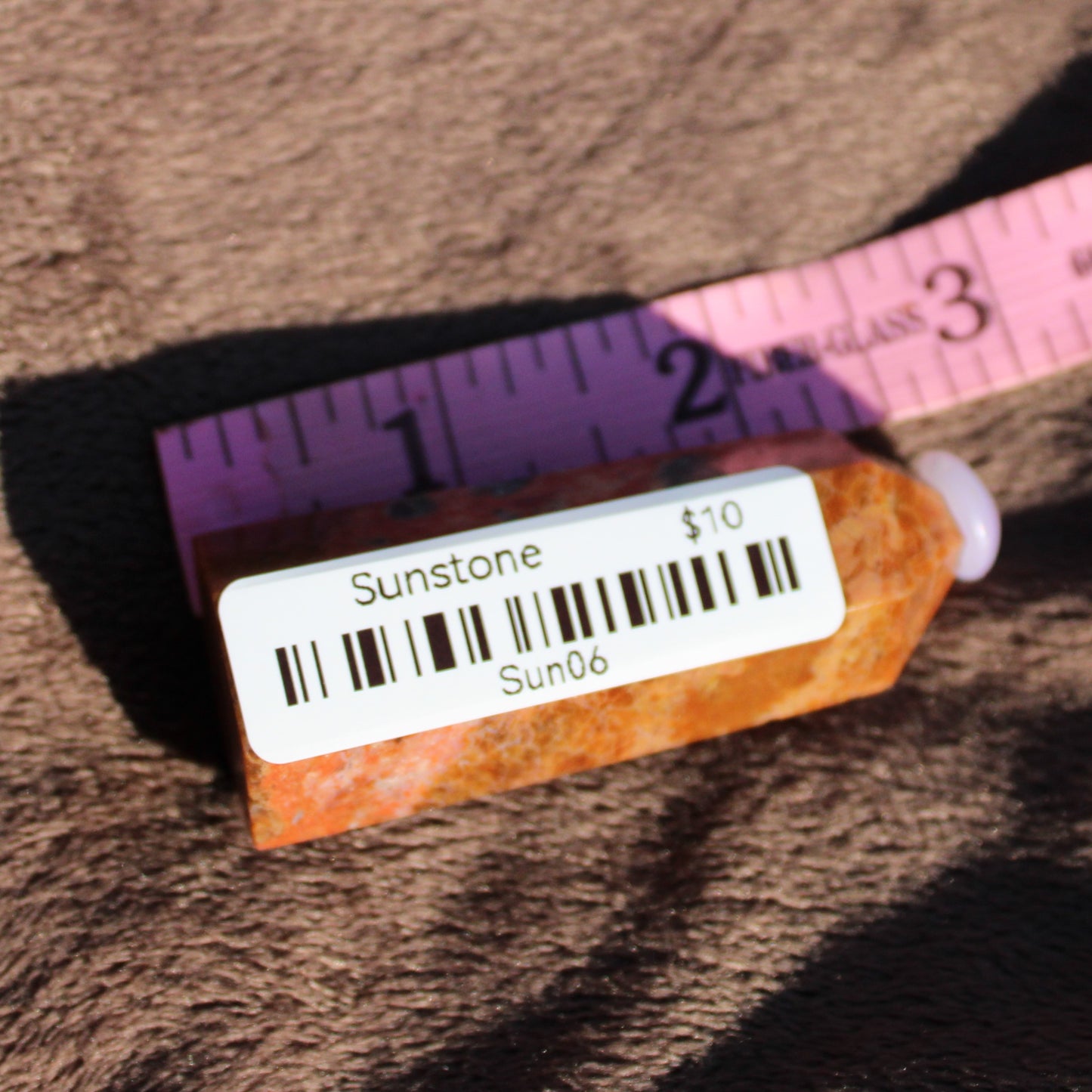 Sunstone tower crystal displayed beside a ruler for size reference with a price tag