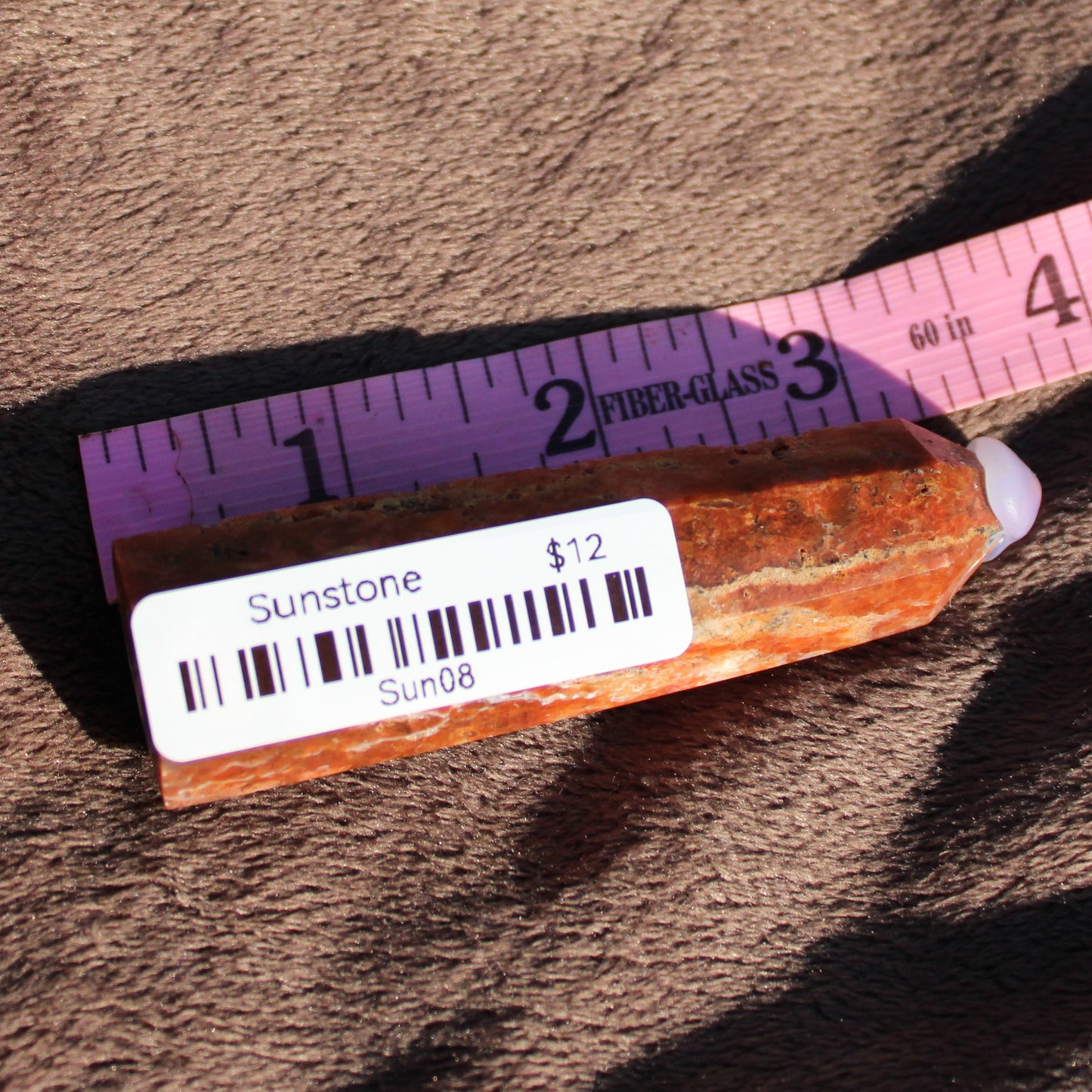 Natural Sunstone tower with orange hues displayed next to a ruler for size reference