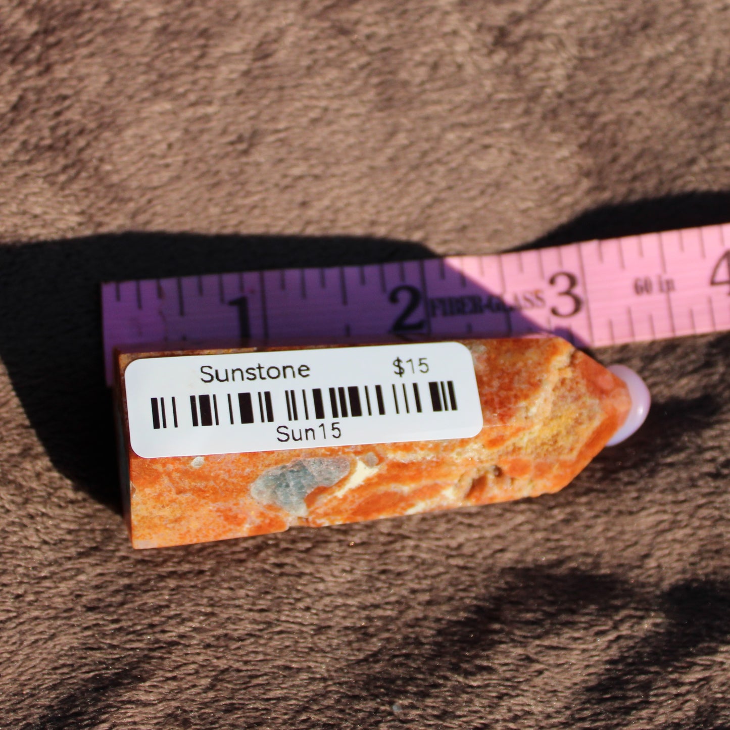 Sunstone tower with vibrant orange hues displayed on a measuring tape for size reference