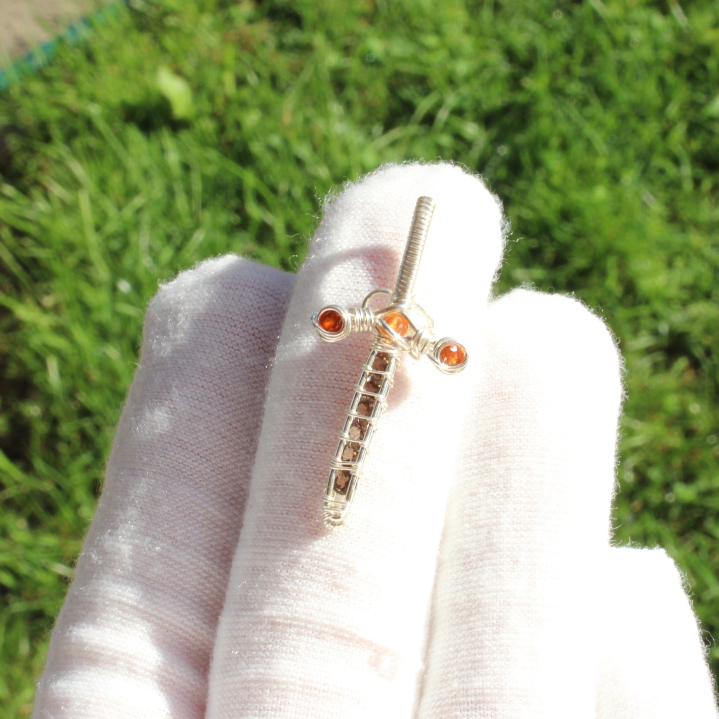 Sword pendant - Smokey quartz, garnet, sterling silver showcased on a hand with a lush green background
