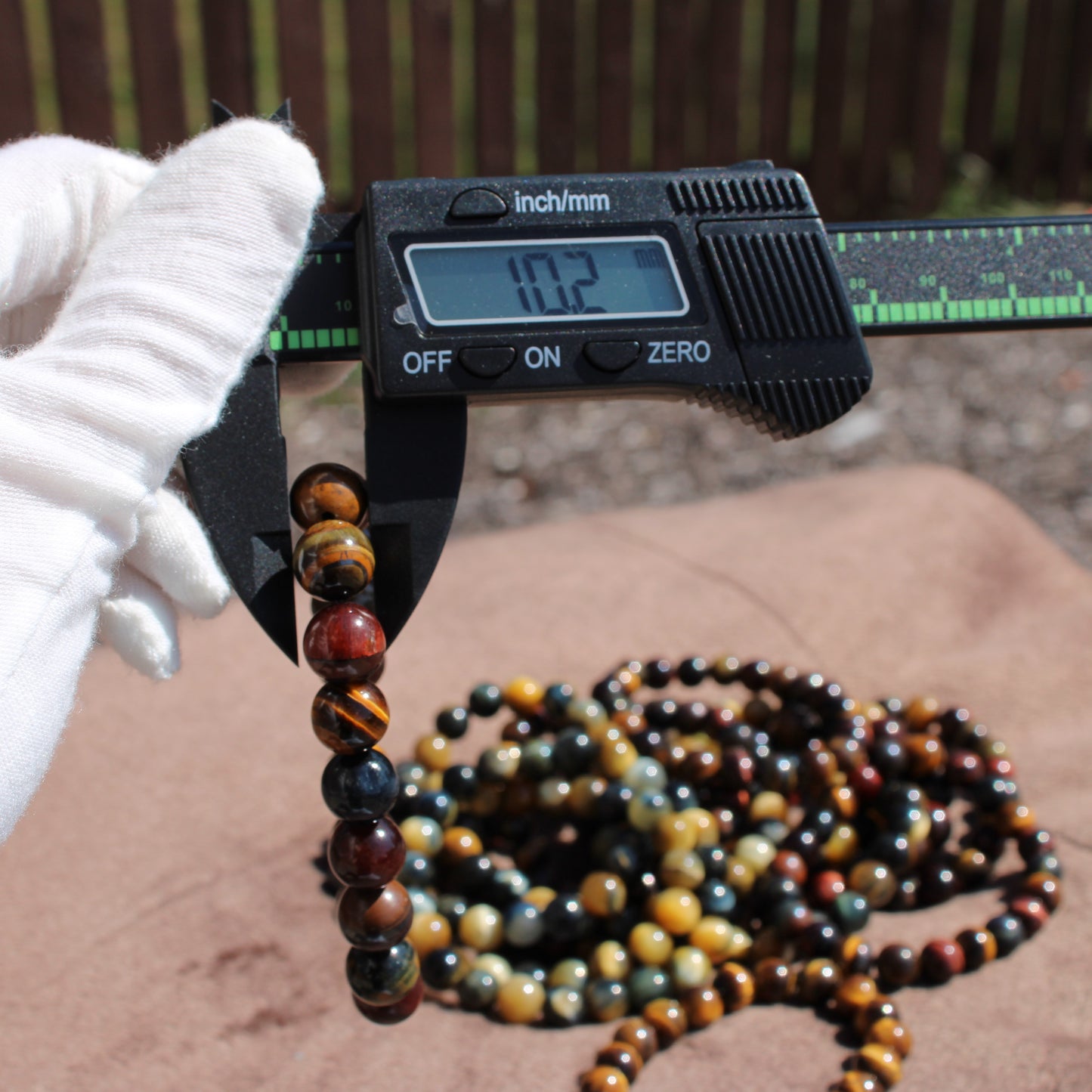 Measuring a Tiger eye Bracelet with calipers, surrounded by other gemstone bracelets
