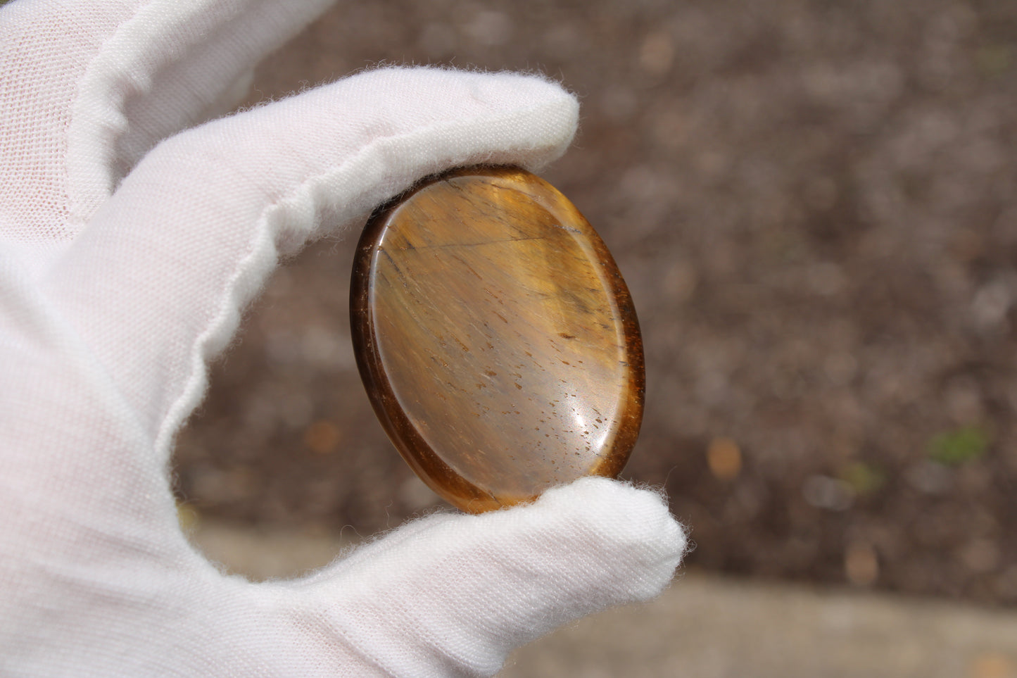 Tiger's Eye worry stone held in a gloved hand with a smooth, polished surface for stress relief