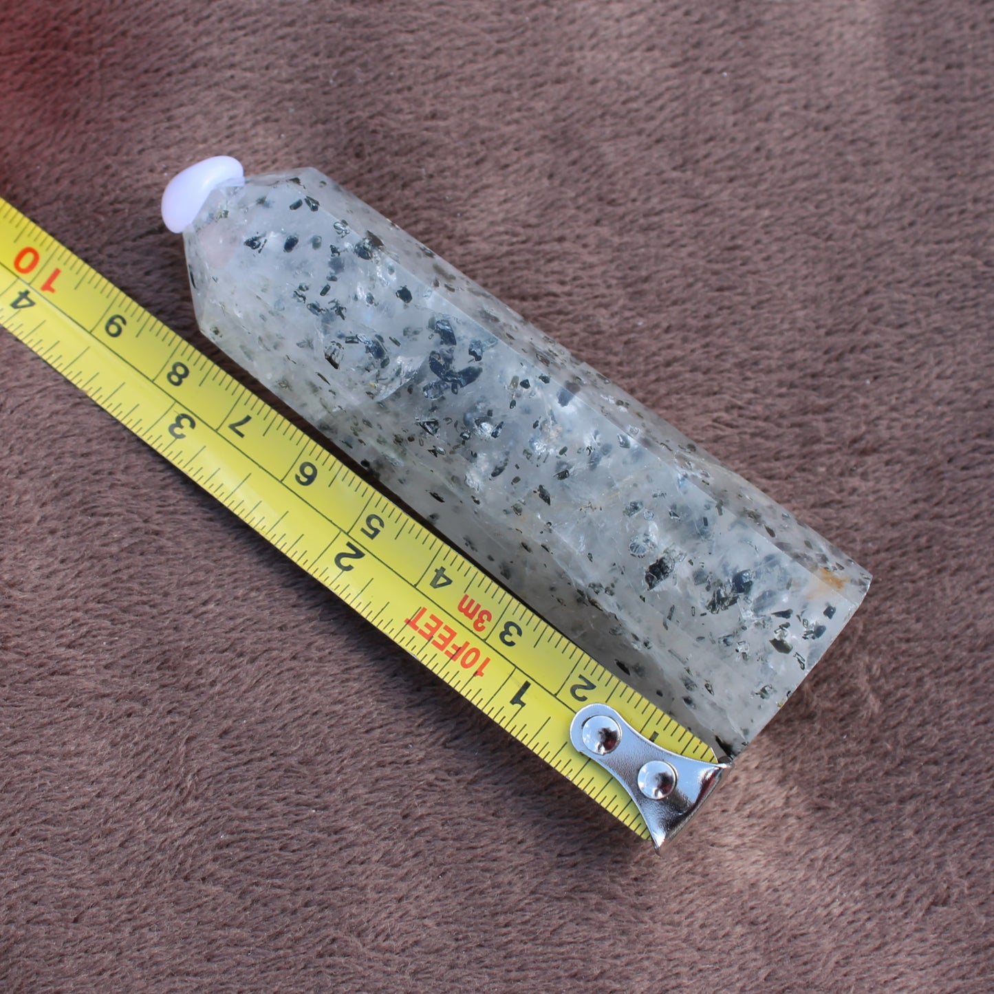 Tourmalited Quartz Tower crystal next to measuring tape showing size on brown fabric