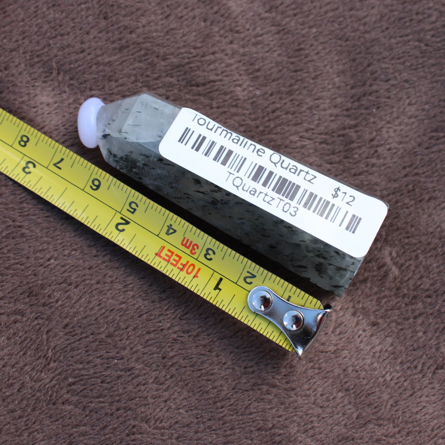 Tourmalited Quartz Tower crystal from Different Branches LLC next to measuring tape on brown surface