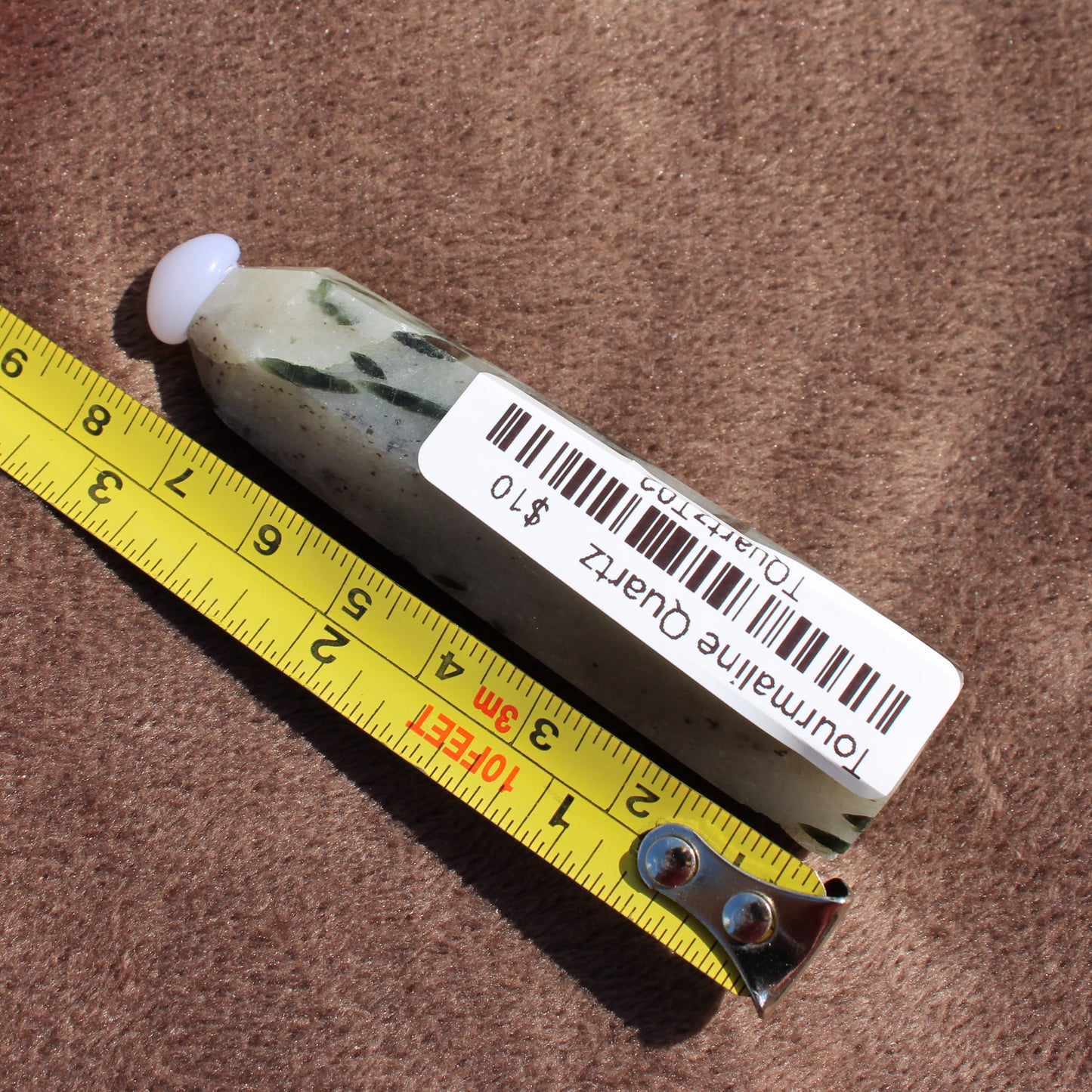 Tourmalited Quartz Tower crystal from Different Branches LLC next to yellow measuring tape on brown fabric