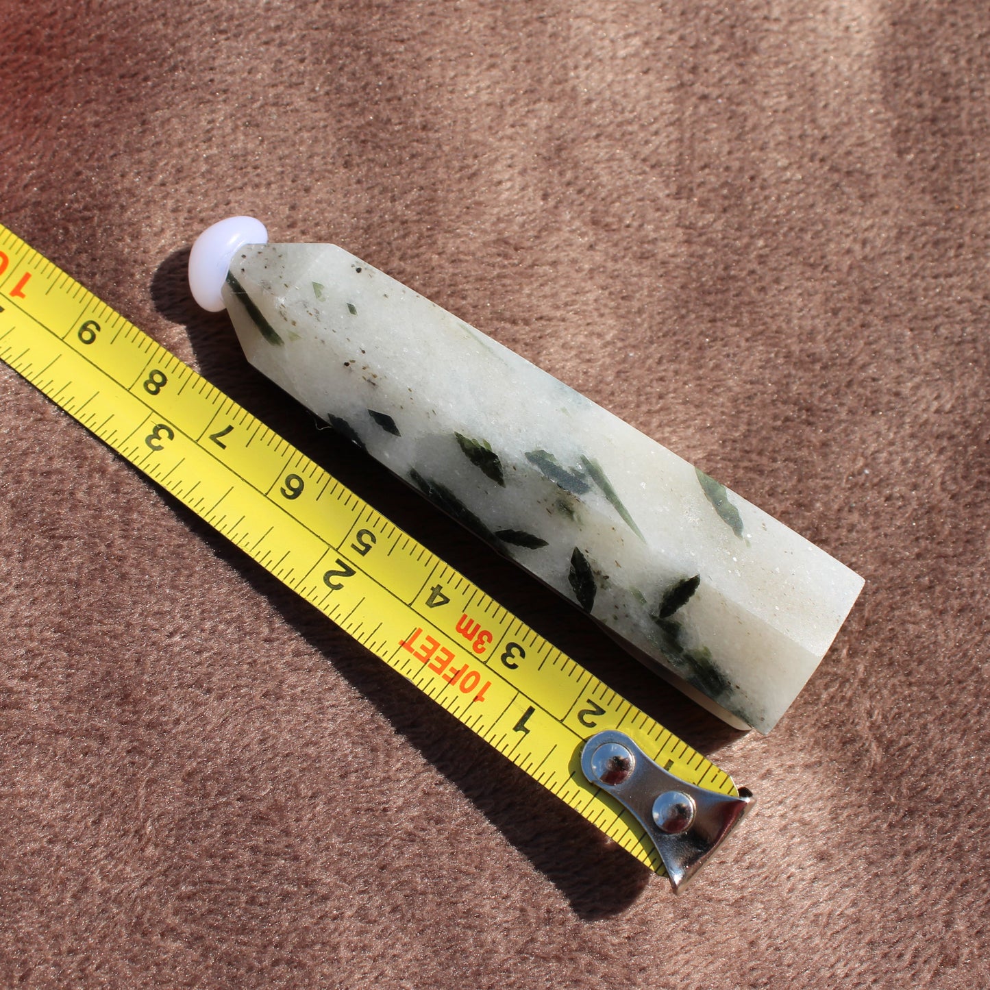Tourmalited Quartz Tower crystal from Different Branches LLC next to measuring tape on brown fabric