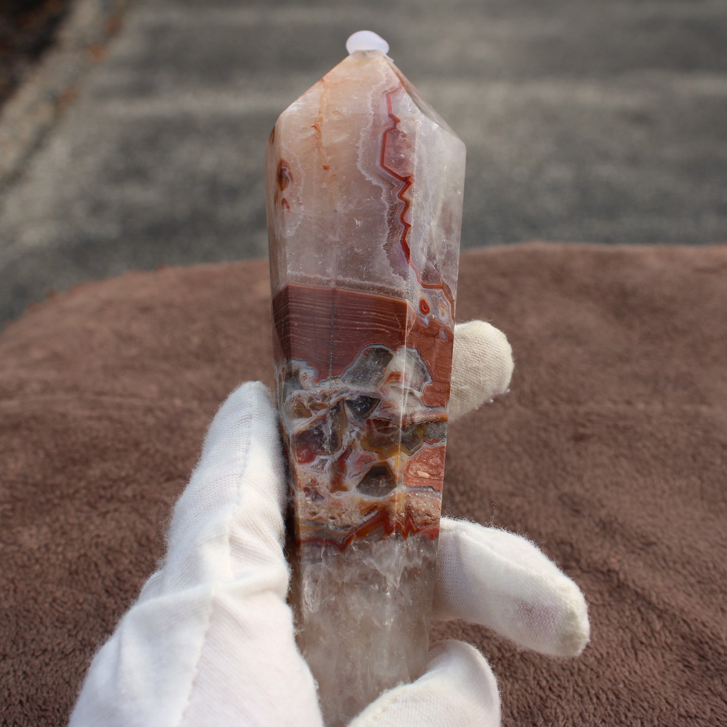 Hand holding a polished Crazy Lace Agate Wand crystal with intricate brown and white patterns
