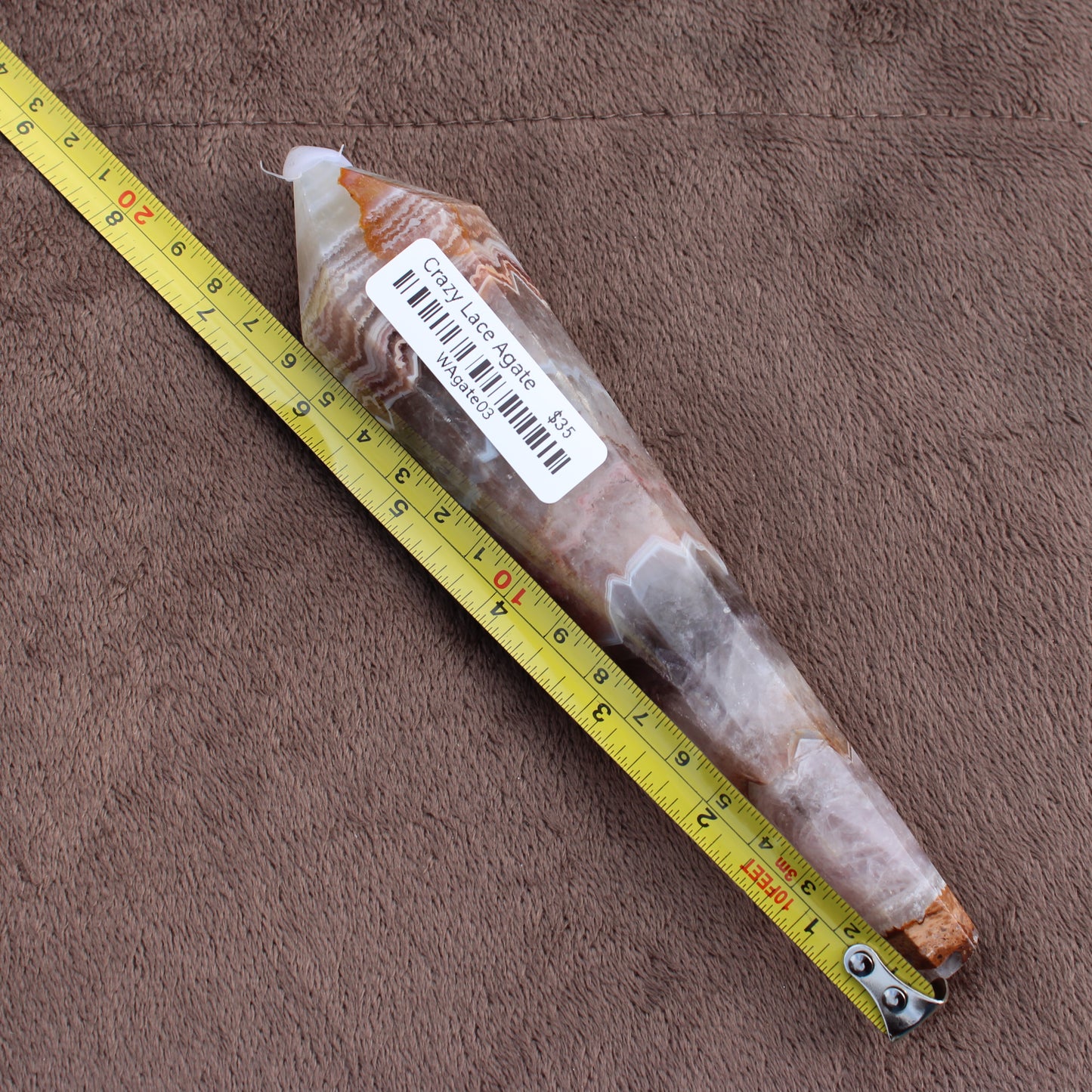 Crazy Lace Agate Wand crystal from Different Branches LLC placed beside a measuring tape on brown fabric