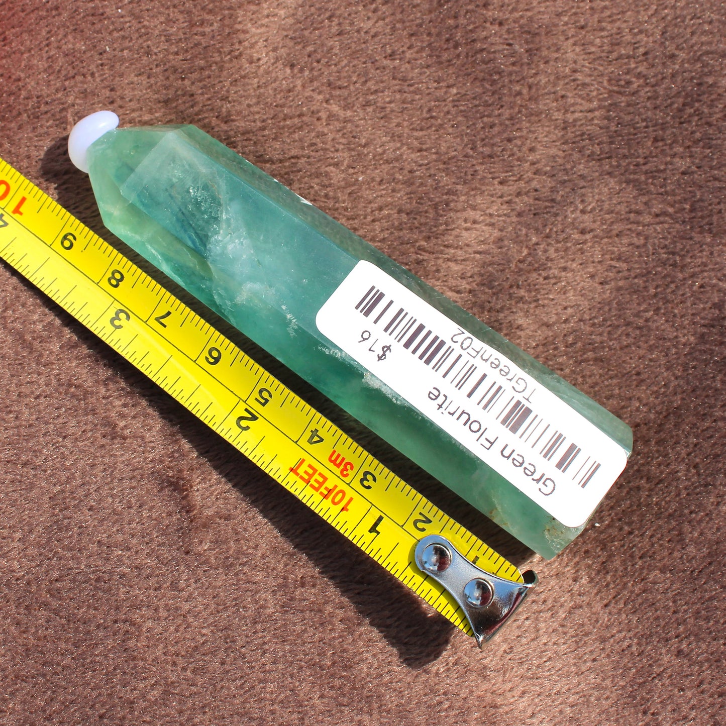 Green Fluorite Tower crystal from Different Branches LLC measured next to yellow tape measure on brown surface