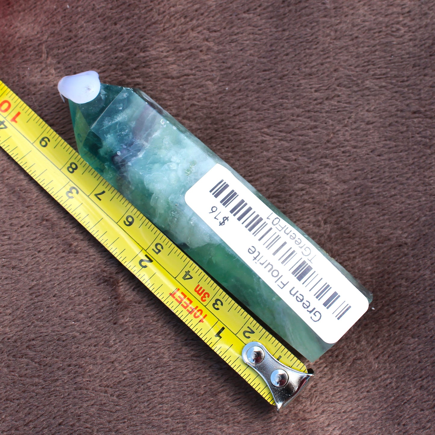 Green Fluorite Tower crystal from Different Branches LLC next to a measuring tape on brown fabric