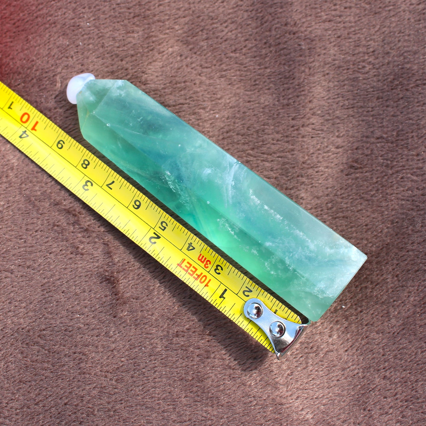 Green Fluorite Tower crystal from Different Branches LLC placed next to a yellow measuring tape on brown fabric
