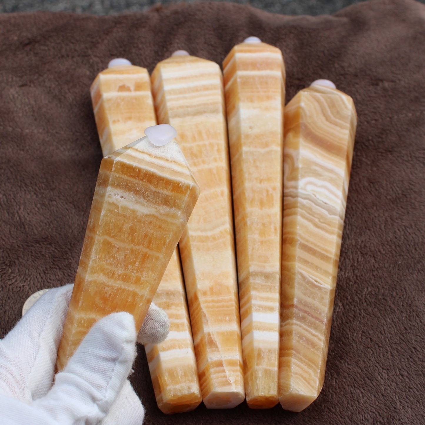 Honey Calcite Wand crystal with orange and white banded pattern held in white glove
