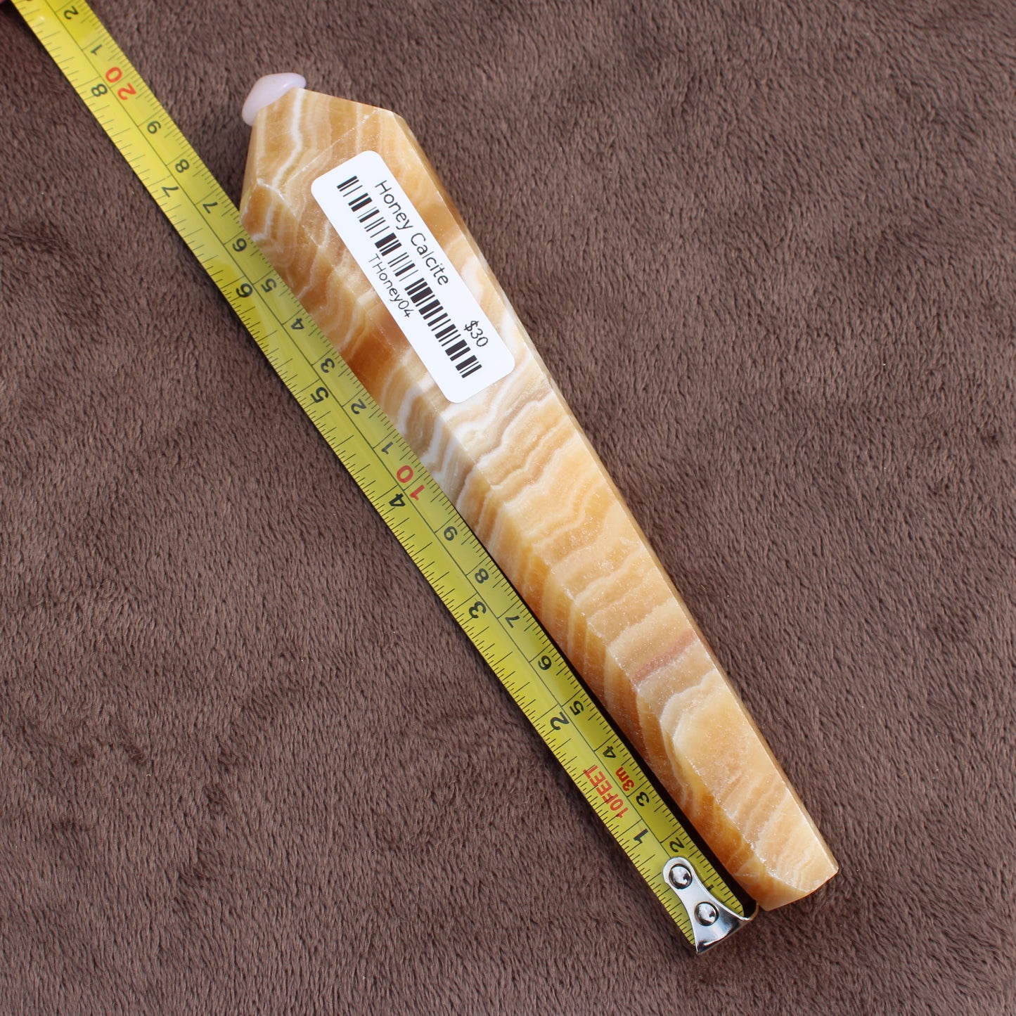 Honey Calcite Wand from Different Branches LLC with yellow and white banded crystal next to measuring tape