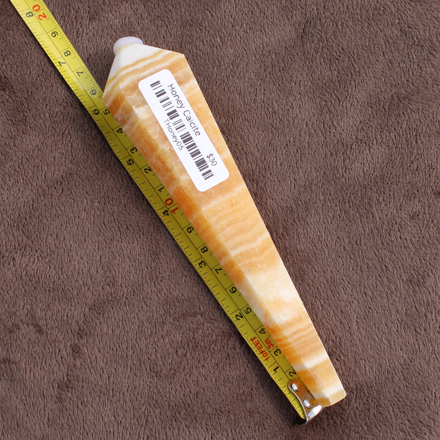 Honey Calcite Wand crystal displaying creamy yellow and white bands with a measuring tape on brown surface